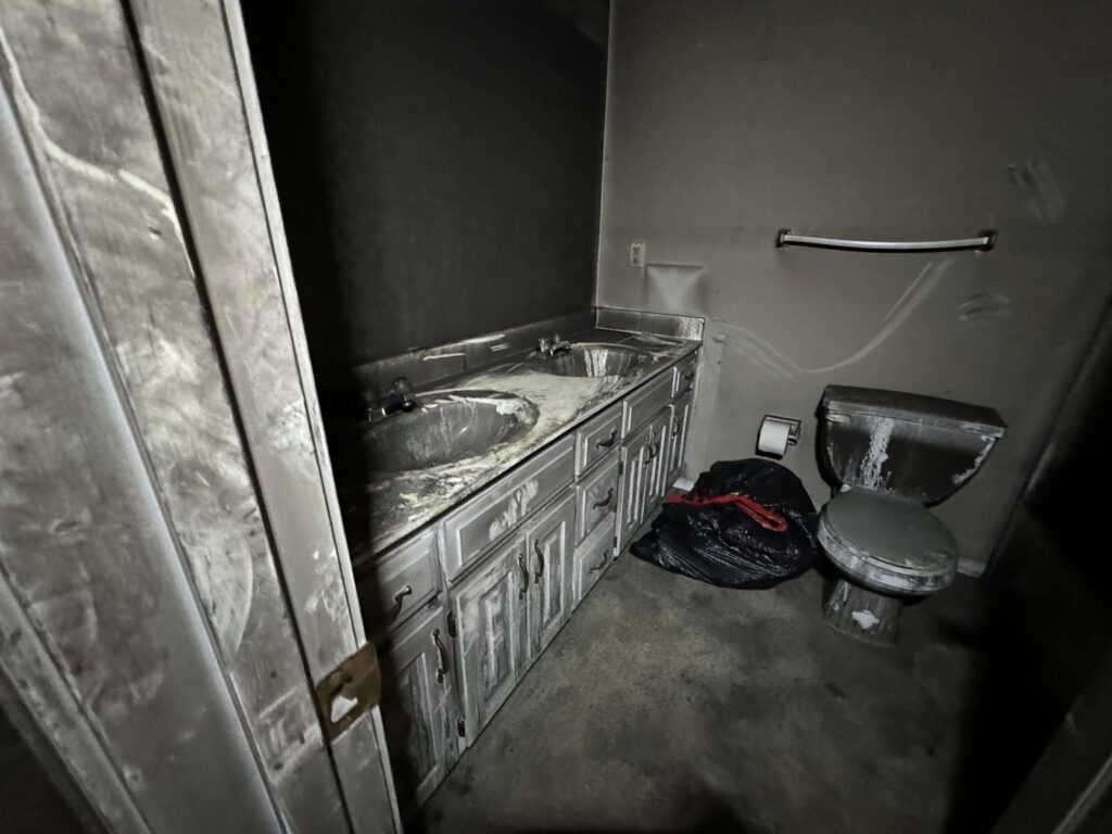 bathroom interior with walls, dual-sink vanity, and toilet heavily covered in black soot after a fire.