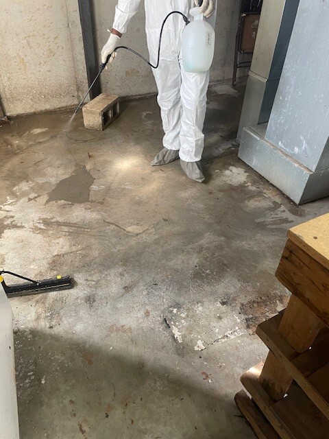 Restor KC technician in protective suit applying antimicrobial to a basement floor