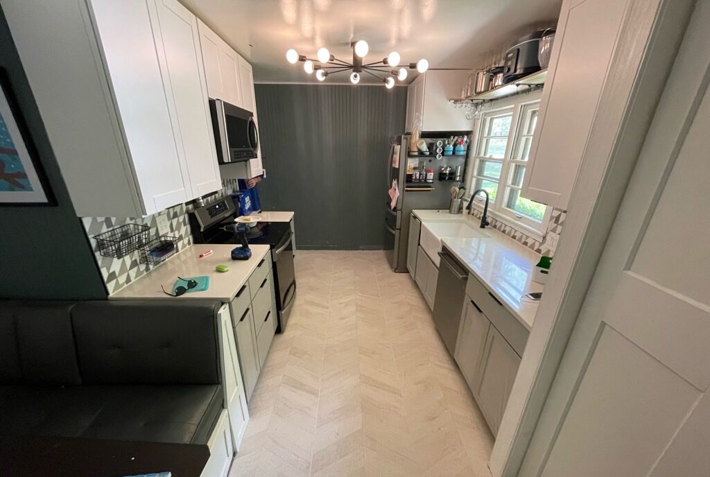 Galley kitchen with new herringbone floor and white cabinets by Restor KC